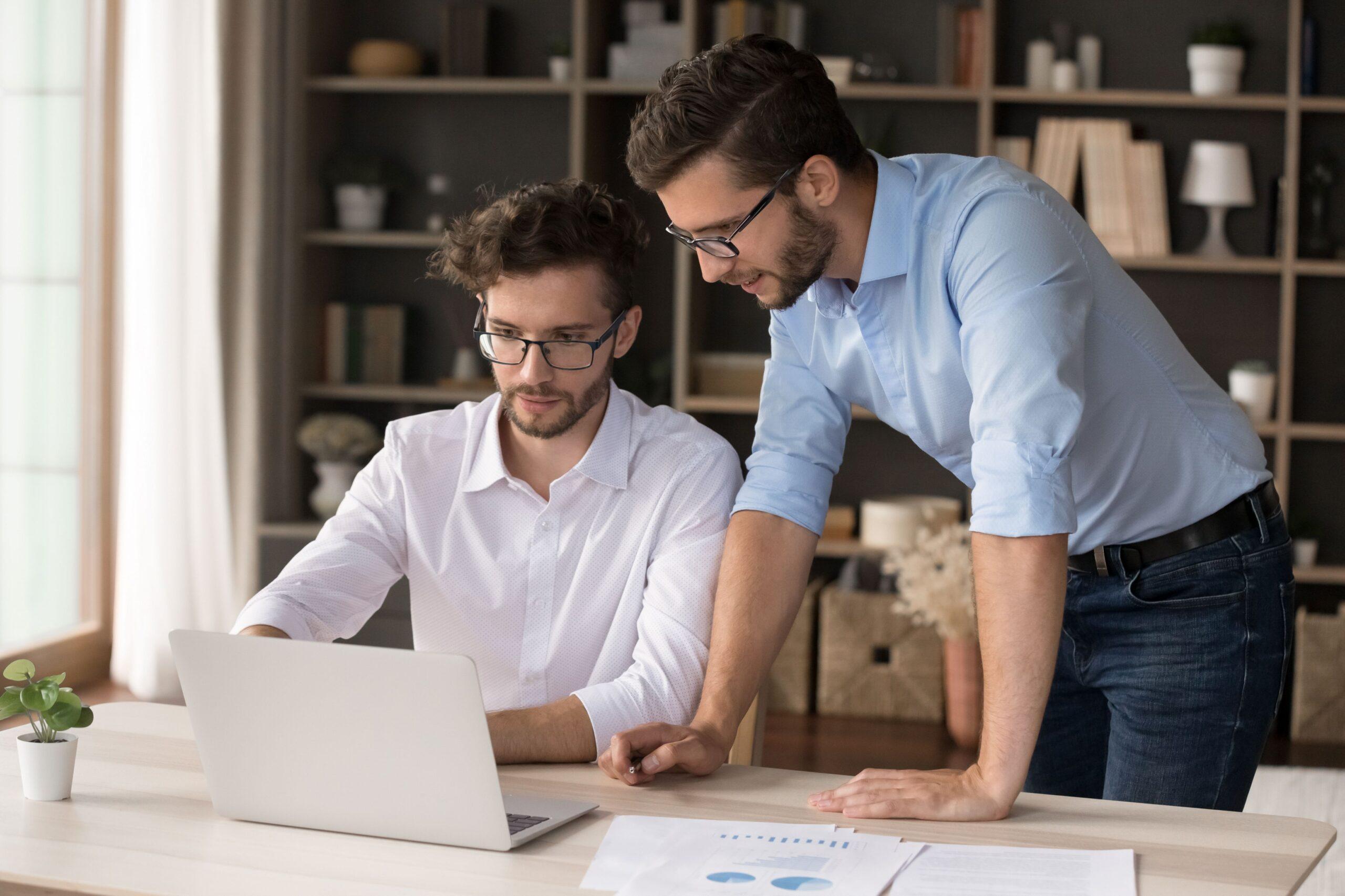 Zwei Männer besprechen betriebswirtschaftliche Daten am Laptop – Symbolbild für Investitionen in Familienservice durch Unternehmen